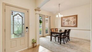 A dining area with a table and chairs, a door with a stained glass design, and a ceiling light fixture. - The Knob Cozy Home (McKinney)
