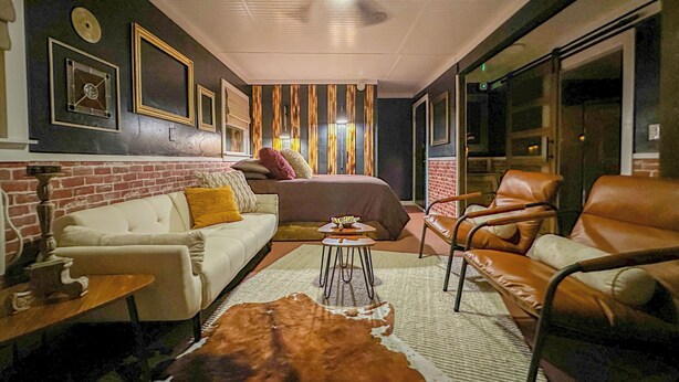 Una habitación de hotel moderna con una cama, un sofá, un sillón de cuero, una mesita y un tapete de cuero de vaca.
