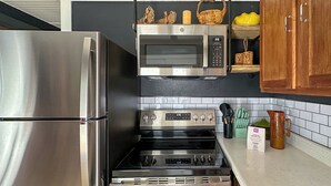 Una cocina con un refrigerador de acero inoxidable, un microondas, una estufa y un horno. Hay armarios de madera y un salpicadero de azulejos.