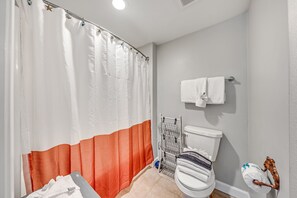 A bathroom with a shower curtain, a toilet, a towel rack, and a shelf with toiletries.