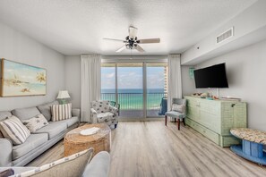 A living room with a sofa, armchairs, a television, and a balcony with a view.