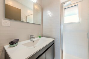 A bathroom with a white sink, a mirror, a towel, and a shower.