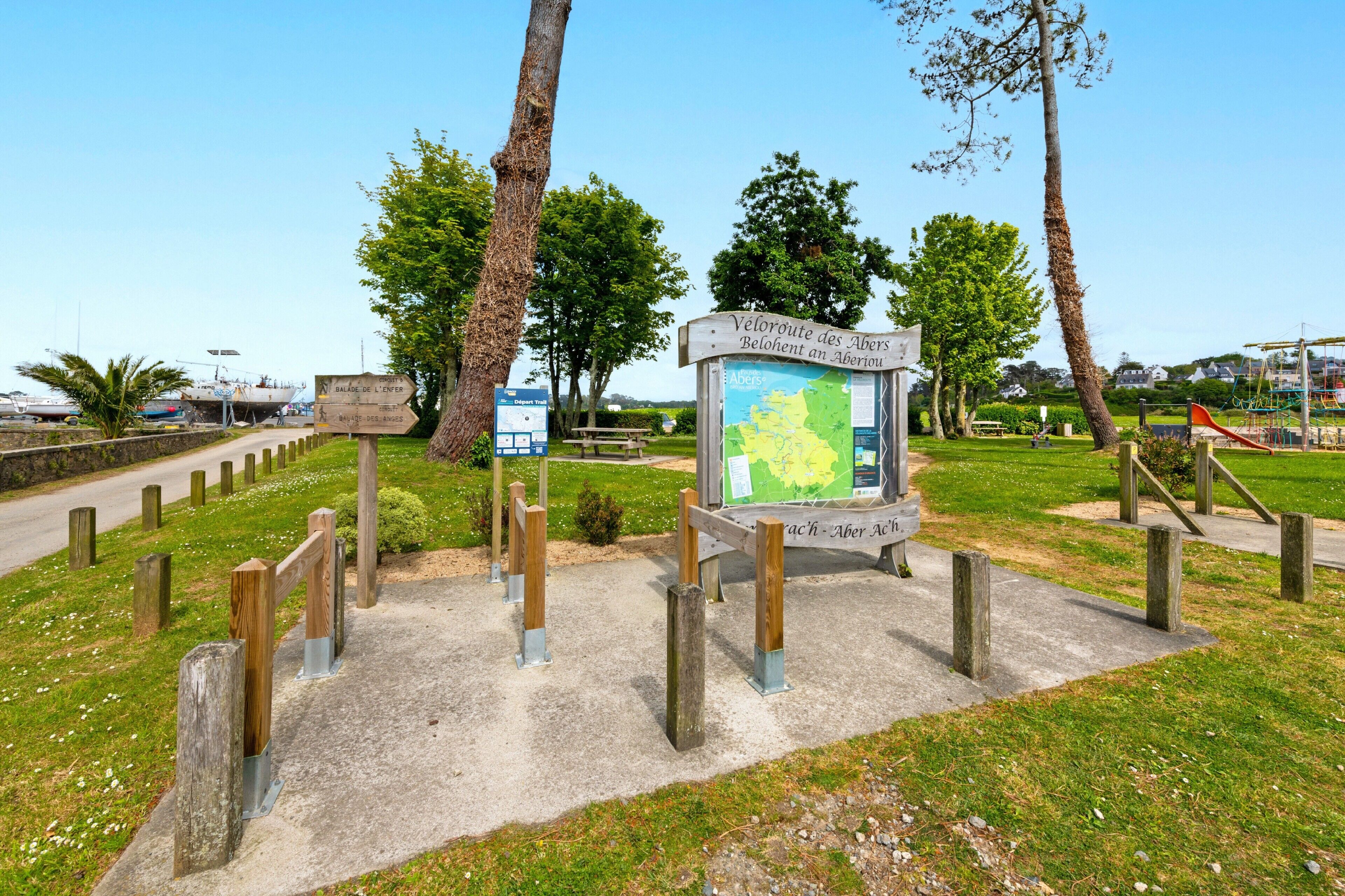 A park with a map sign, wooden fence, and trees.