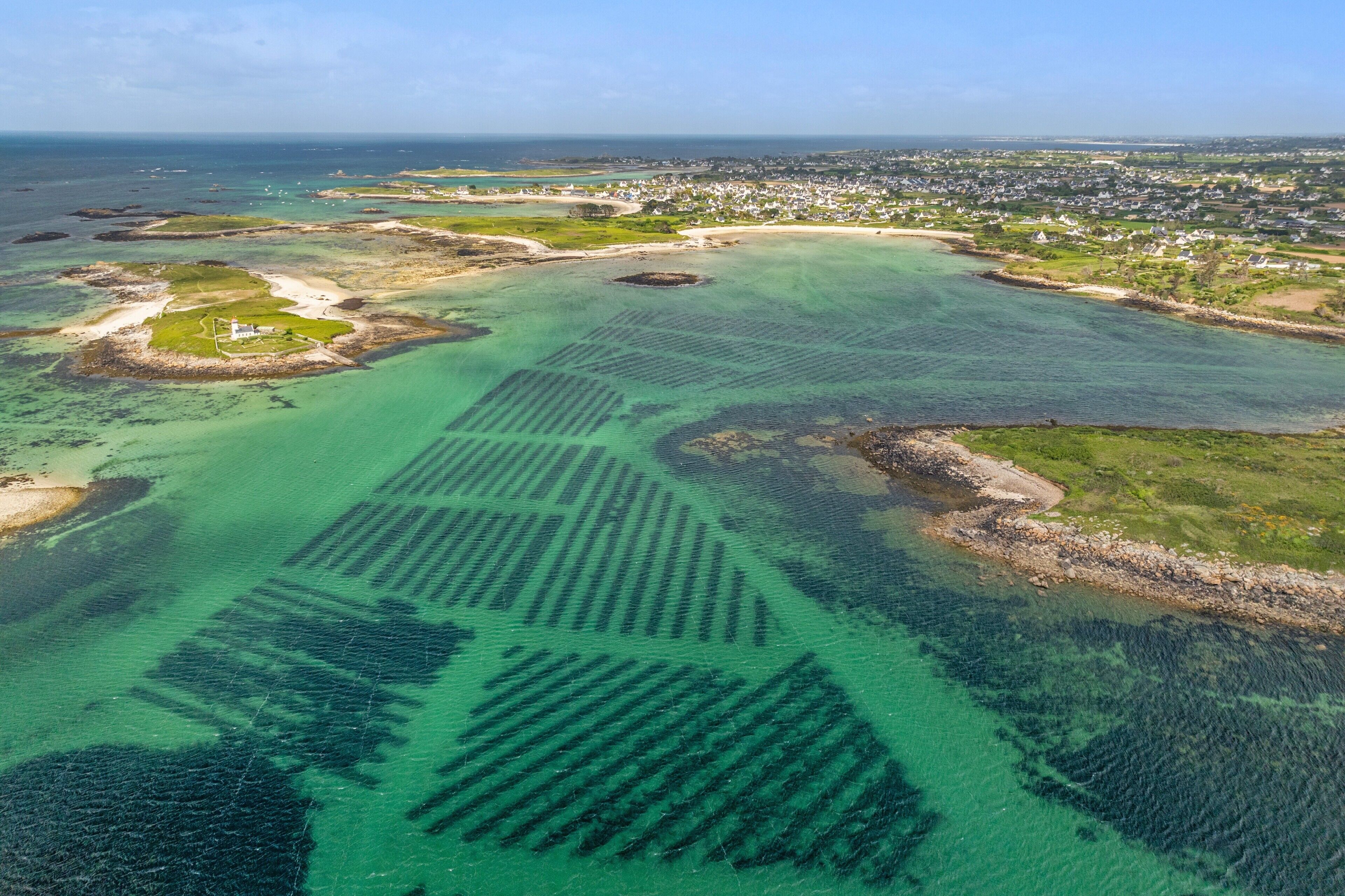 Luchtbeeld van een kustgebied met helder water, een vuurtoren en een woongebied.