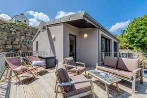 A deck with outdoor seating, a stone wall, and a building with a satellite dish.