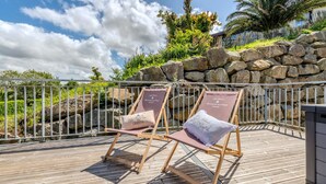 Two wooden deck chairs with cushions labeled 'LANDÉDA' and 'ST. BARTOLOMÉ' on a wooden deck with a stone wall and palm trees in the background.