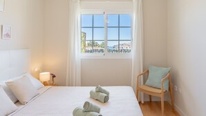Une chambre à coucher avec un lit, une chaise, une fenêtre avec des rideaux et une vue sur des immeubles.