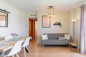 A modern living room with a grey sofa, a dining table with chairs, a pendant light, and a wall-mounted shelf with a plant. - Apartment 'Sea Views - 2 Bedrooms' with Shared Pool, Wi-Fi and Air Conditioning (Benalmádena)