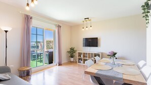 Un salon moderne avec un coin repas, de grandes portes-fenêtres coulissantes donnant sur un balcon, un téléviseur à écran plat et une plante en pot.