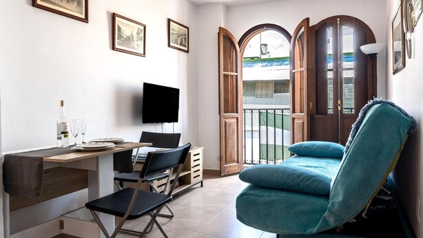 Une pièce comprenant un bureau, une chaise, un téléviseur et offrant une vue sur un bâtiment, visible à travers une porte.