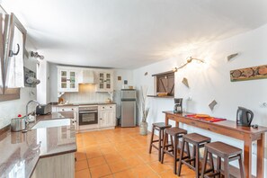 Eine Küche mit weißen Schränken, einem Kühlschrank, einer Kaffeemaschine und einer Holztresen mit Hockern.