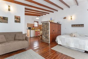 Ein Zimmer mit Holzboden, einer Couch, einem Bett, einer Steinwand, einer Küchenzeile und Kunstwerken an den Wänden.
