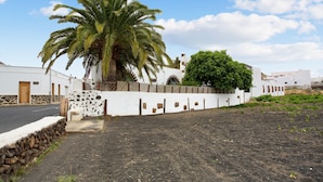 A white building with a stone wall, a palm tree, and a garden area. - Vacation Villa 'Casa Rural La Molina' with Mountain View, Private Terrace and Wi-Fi (Máguez)
