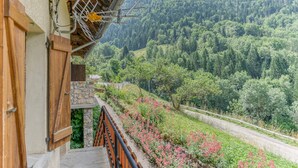 Un balcone con vista su un pendio boscoso, un muro in pietra e una ringhiera in metallo.