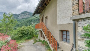 Un edificio con facciata in pietra, un balcone in legno e vista su un paesaggio montuoso.
