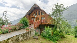 A wooden mountain cabin with a wooden staircase, a stone wall, and a garden with pink flowers. - Apartment 'Passoud 203' with Mountain View, Shared Garden and Wi-Fi (VAUJANY)