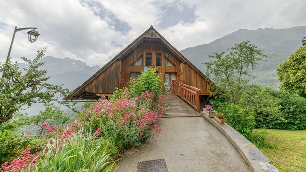 A wooden chalet with a steep roof, a wooden deck, and a pathway leading to the entrance. - Apartment 'Passoud 203' with Mountain View, Shared Garden and Wi-Fi (VAUJANY)