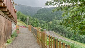 A pathway leading to a building with a wooden fence, surrounded by lush greenery and hills. - Apartment 'Passoud 203' with Mountain View, Shared Garden and Wi-Fi (VAUJANY)