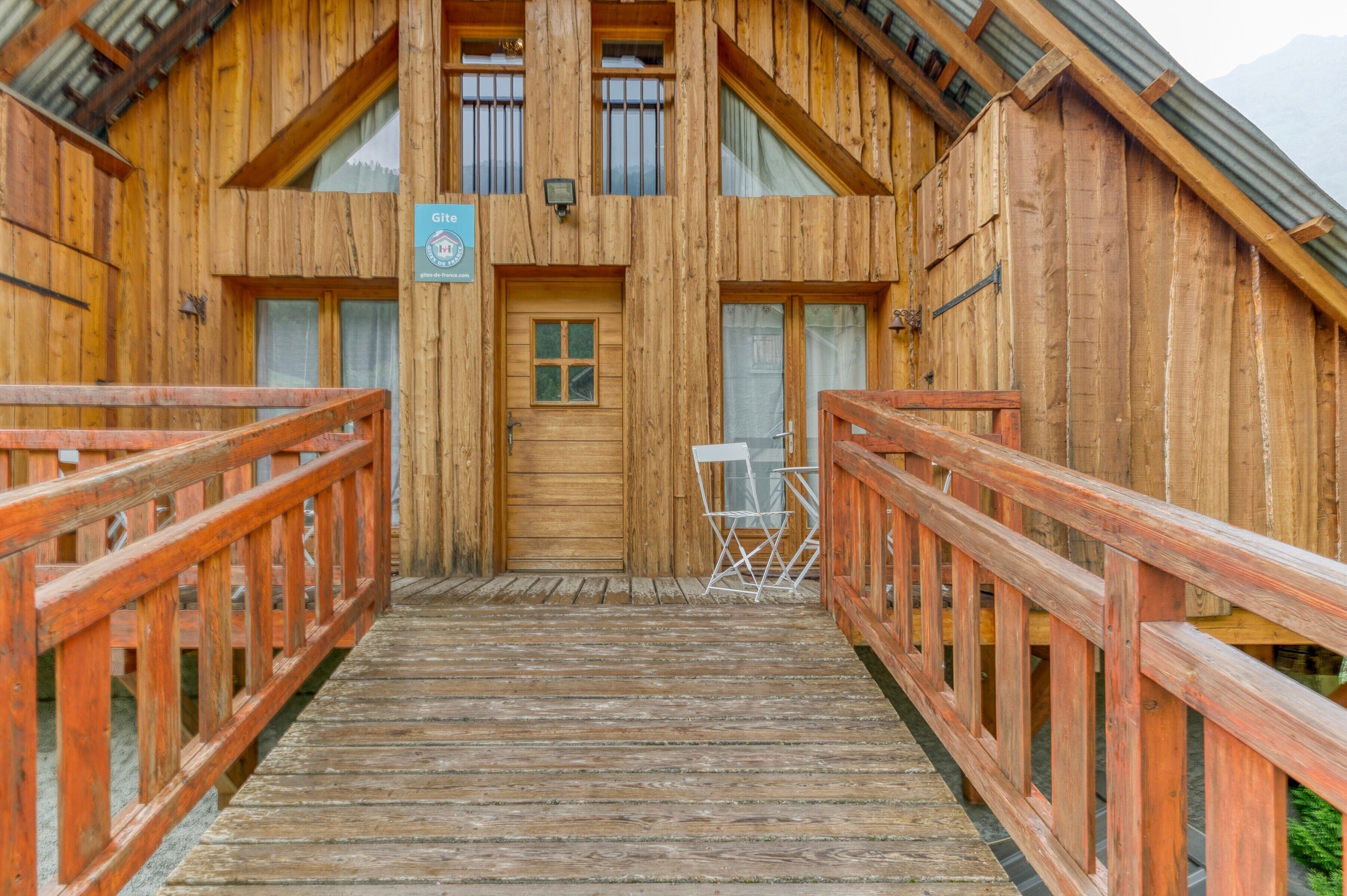 Een houten lodge met een houten trap die naar een deur leidt, een bord boven de deur en een stoel ervoor.