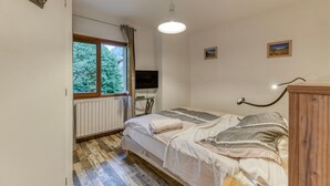 A bedroom with a bed, a window, a radiator, a TV, and a wooden cabinet.