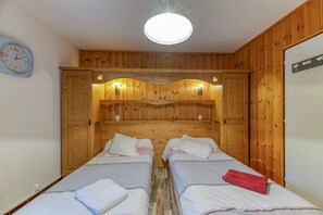 Una habitación con dos camas, paneles de madera, un reloj y una lámpara en el techo.