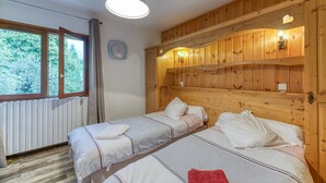 Ein Zimmer mit zwei Betten, Holzwandverkleidung, einem fenster mit Vorhängen, einer Uhr und einer Pendelleuchte.