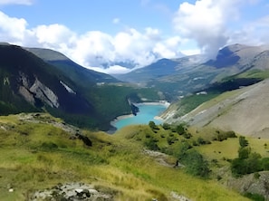 Paisaje montañoso con un lago y un pequeño edificio en el valle.