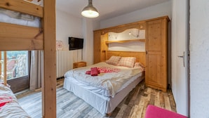 Quarto com cama, guarda-roupa de madeira, televisão e janela com vista.