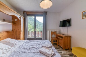 Ein Schlafzimmer mit Bett, einem Holztisch, einem Fernseher und einem Balkon mit Blick auf Grünflächen.
