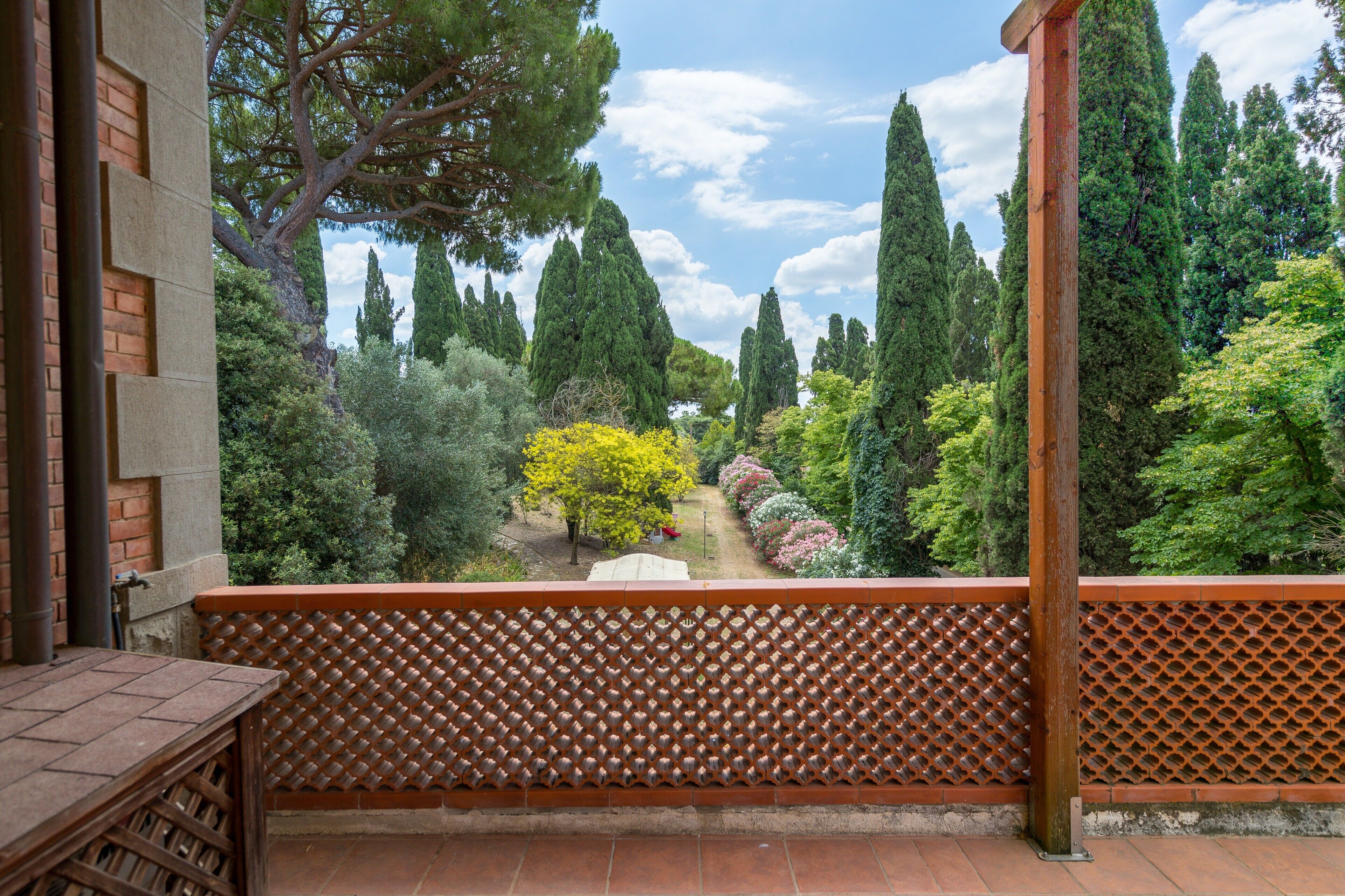 Un balcón con vista a un jardín, un muro de ladrillo y una mesa de madera.