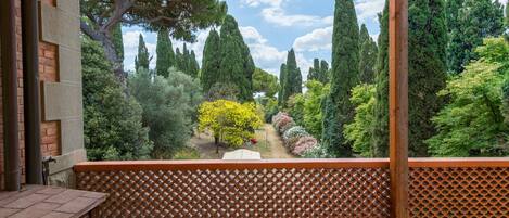 Un balcón con vista a un jardín, un muro de ladrillo y una mesa de madera.
