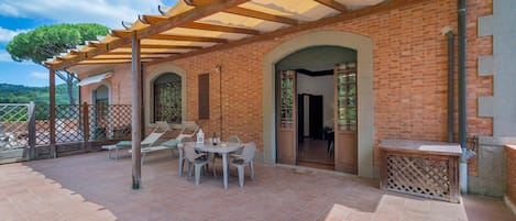 Un patio cubierto con pared de ladrillo, una mesa con sillas y una pérgola de madera.