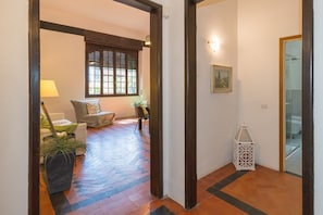 A hallway with a patterned floor, a sofa set, a window with blinds, and a white lantern.