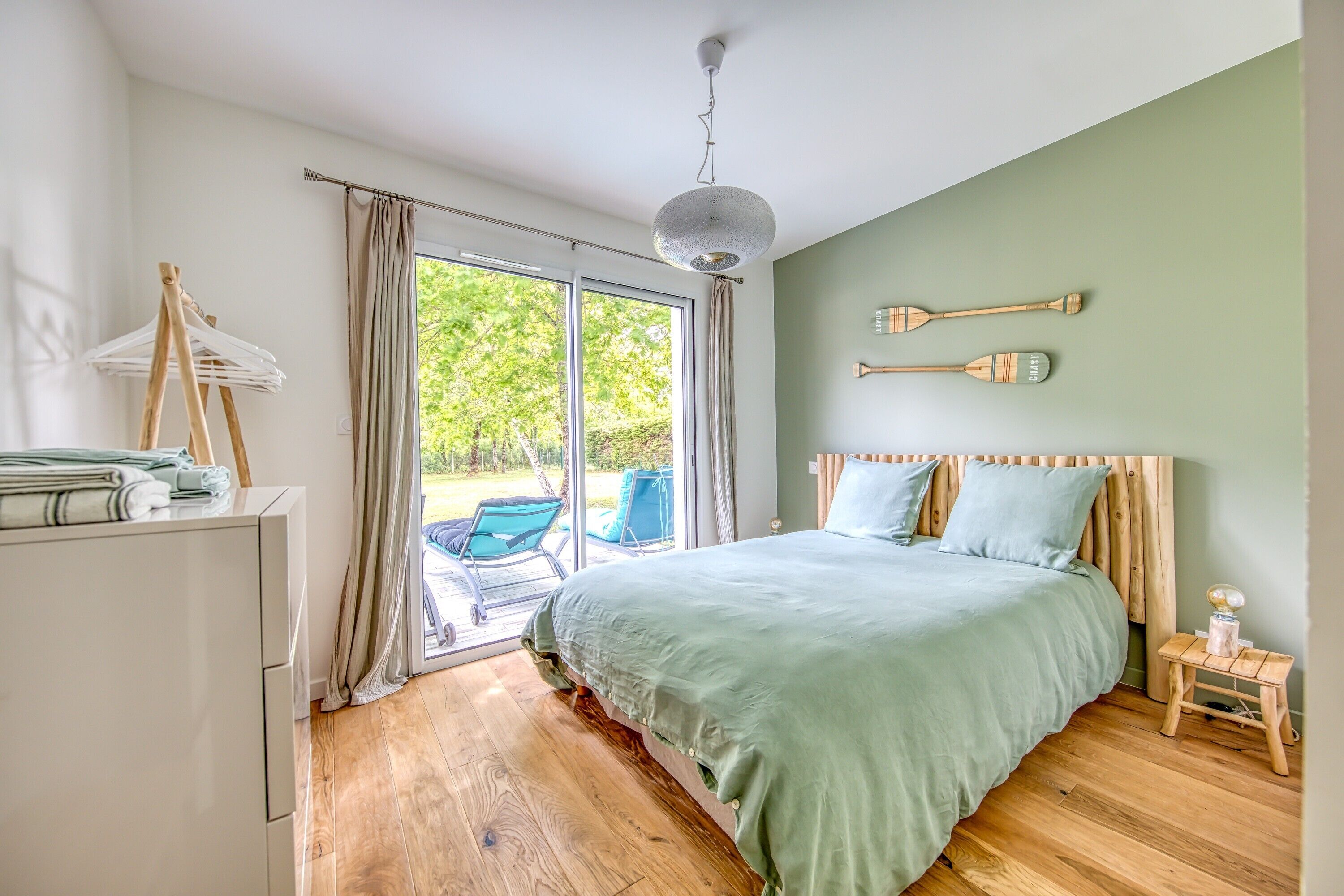 A bedroom with a bed, a wooden dresser, a hanging chair, and a view through a glass door.