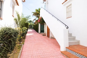 A narrow pathway leading to a white building with a staircase.