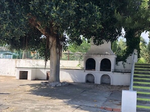Une cour avec un arbre, un mur blanc orné d’arches et une clôture en métal.