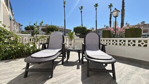 Two lounge chairs with striped cushions, a small table, and a white fence with decorative elements.