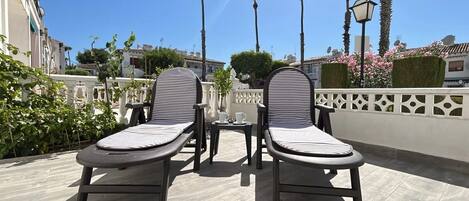 Two lounge chairs with striped cushions, a small table, and a white fence with decorative elements.