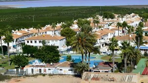 A resort with multiple white buildings, a swimming pool, and palm trees.