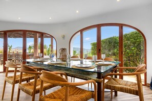 A dining area with a glass table, wicker chairs, and a view of greenery and mountains. - Villa 'Caroix' with Sea View, Wi-Fi and Air Conditioning (Xàbia)