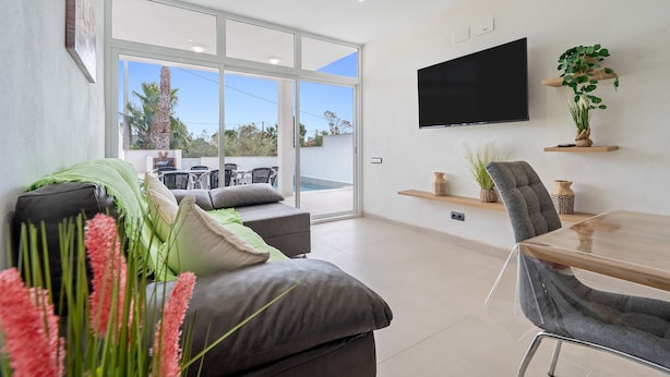 A modern living room with a sofa, a dining table, a TV, and a large window.