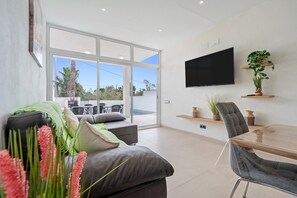 A modern living room with a sofa, a dining table, a TV, and a large window.