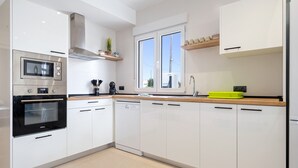 A modern kitchen with white cabinets, a microwave, oven, dishwasher, and a window with a view.