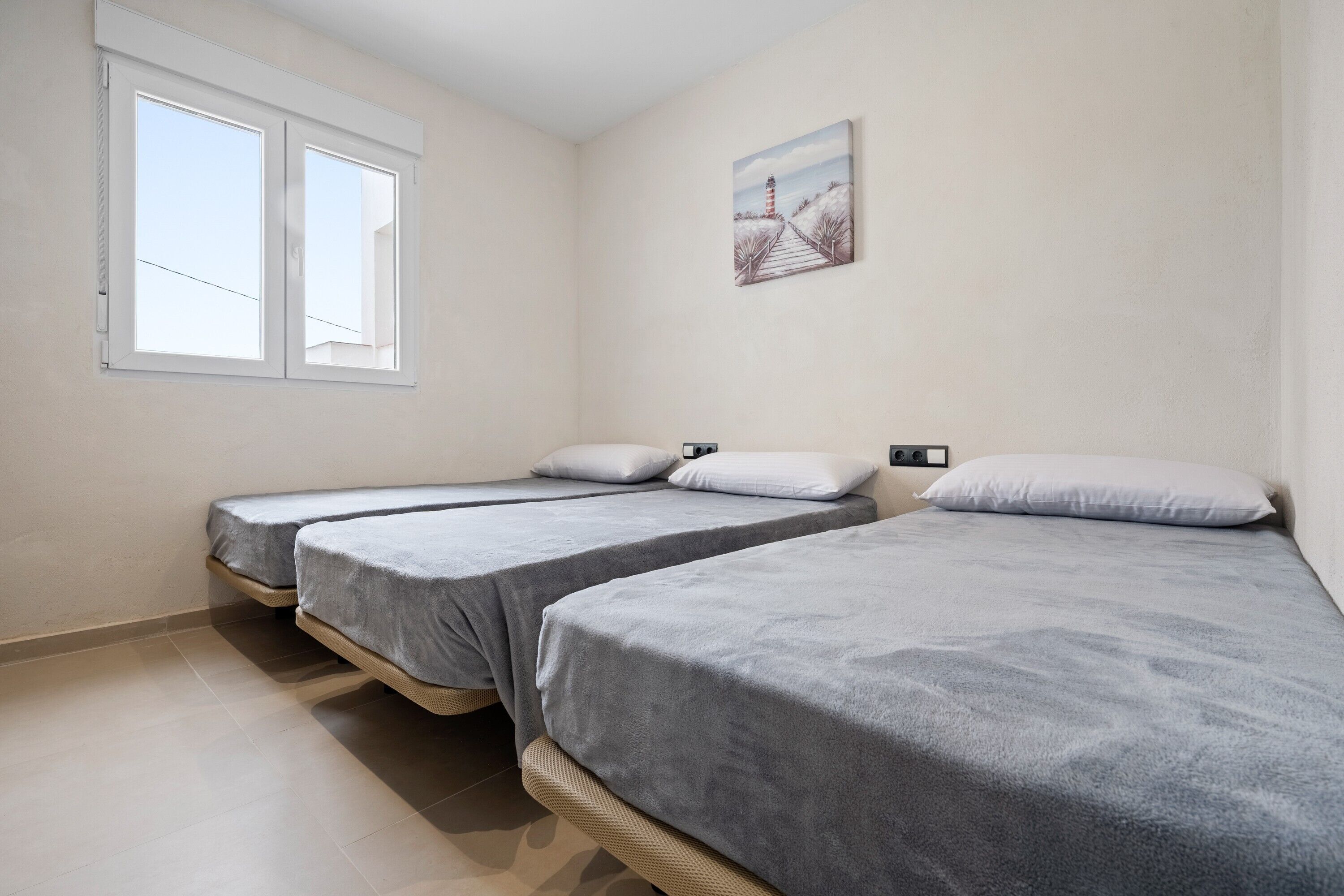A room with three single beds, a window, and a painting on the wall.