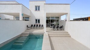 A modern building with a swimming pool, outdoor seating, and a clear sky.