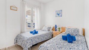 Une chambre avec deux lits, une table de chevet, une lampe et une fenêtre avec des rideaux.