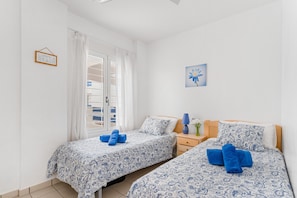 A bedroom with two beds, a nightstand, a lamp, and a window with curtains.