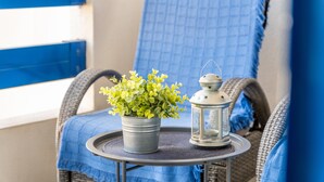 Une chaise en osier avec un coussin bleu, une petite table ronde ornée d’une plante en pot et d’une lanterne, et un mur bleu en arrière-plan.