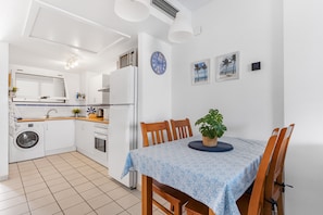 A compact kitchen with a washing machine, a dining table with chairs, and a clock on the wall.