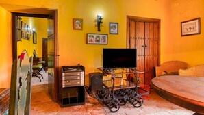 A room with a bed, a television on a stand, a wooden door, and a wall with framed pictures.